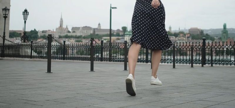 devojka veselo trči po gradu obučena u suknju i bele patike
