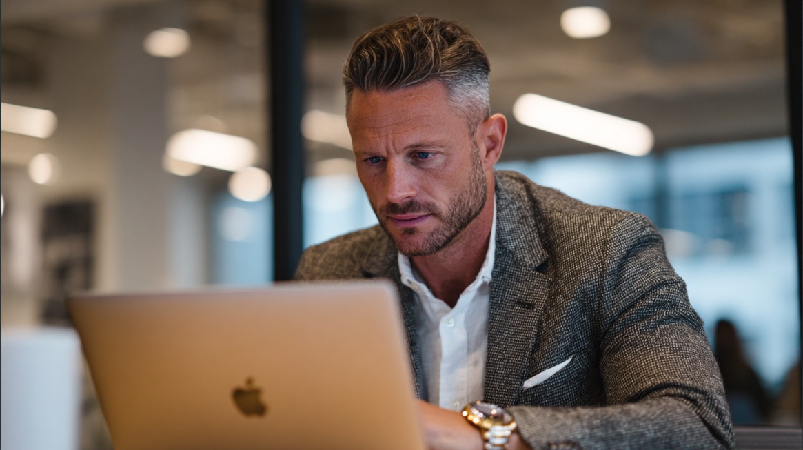 Muškarac u odelu sedi za laptopom u modernoj kancelariji i koncentrisano radi