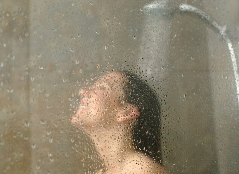 blurovan prikaz devojke pod tušem i kapljice vode okolo